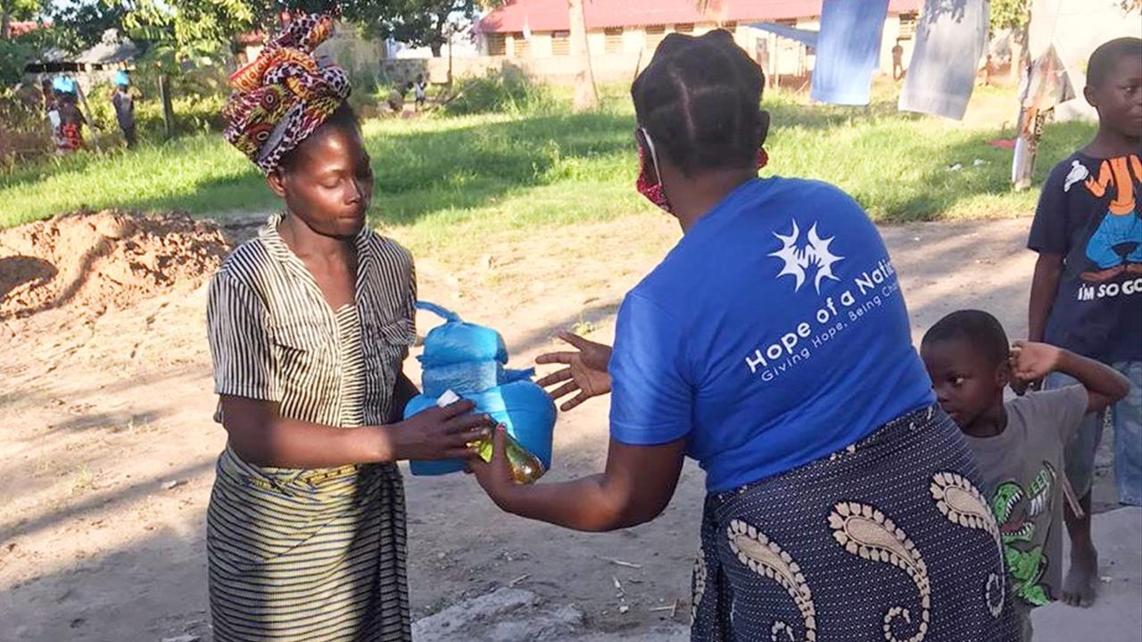 A Hope of a Nation team member handing a relief gift to a woman as children look on