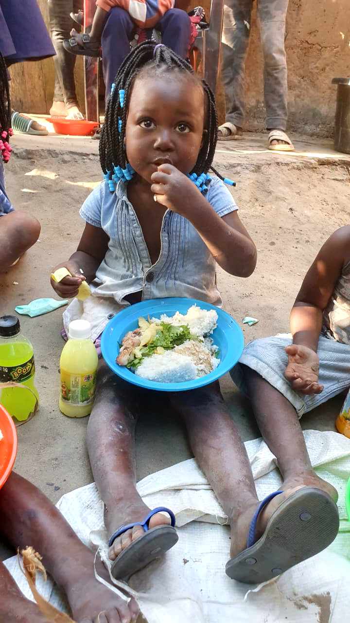 A young girl eating a plate of rice, greens, and meat while sitting with other children at a weekly gathering in Mozambique