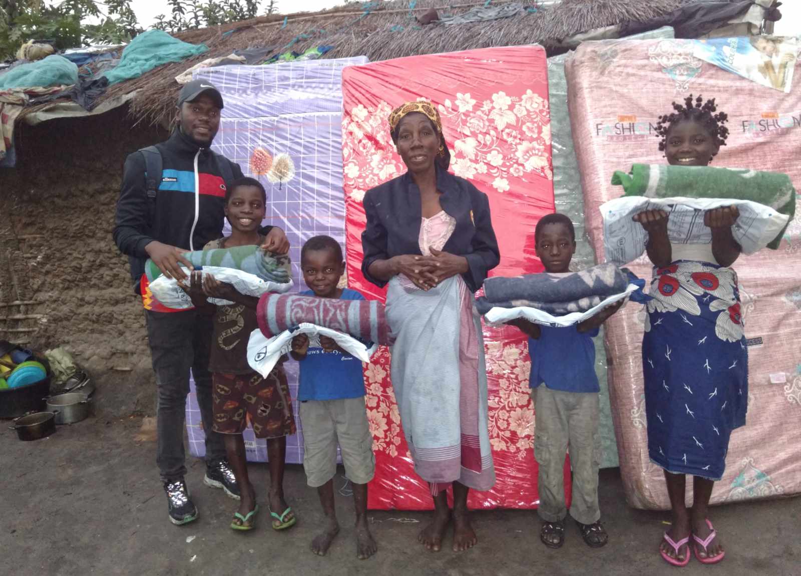 Tony with some of our children and their grandmother caring for them, holding new blankets beside the mattresses they received.
